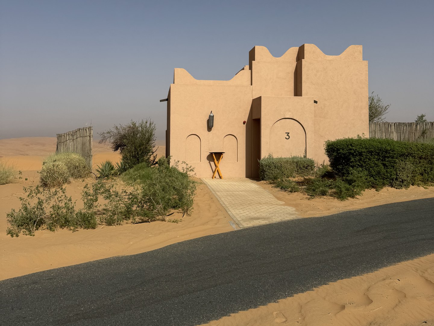 Sand-coloured villa with crenellated walls at Bab Al Nojoum Bateen Liwa, set among desert shrubs and dunes